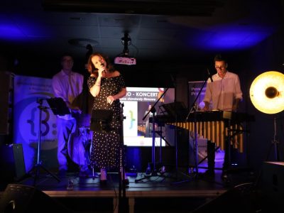 Zespół Joanna Bejm Trio występuje na scenie w kameralnej sali. Na środku stoi wokalistka w czarnej sukience odsłaniającej ramiona i śpiewa do mikrofonu. Po bokach towarzyszą jej muzycy grający na kontrabasie oraz wibrafonie. Po obu stronach sceny stoją duże, okrągłe lampy emitujące ciepłe, żółte światło, a tło jest rozświetlone niebieską poświatą