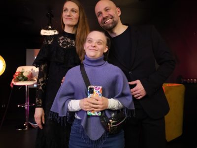 Natalia Srokocz i Jerzy Grzechnik pozują na scenie z dziewczyną w fioletowym ponczo, która trzyma w dłoniach smartfon w kolorowym etui i patrzy z uśmiechem w górę. Po lewej stronie w tle widać bukiet kwiatów leżący na krześle barowym