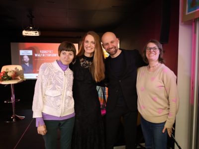Pamiątkowe zdjęcie ze spotkania. Wokalistka Natalia Srokocz w czarnej koronkowej sukience i wokalista Jerzy Grzechnik w czarnej marynarce pozują na scenie objęci z dwiema uczestniczkami wydarzenia. W tle widoczny ekran z plakatem „Koncert Walentynkowy”