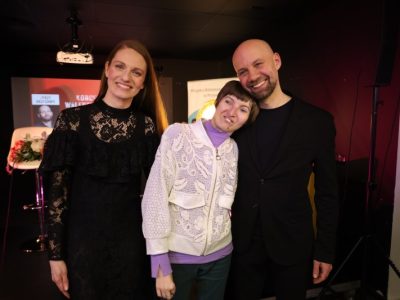 Pamiątkowa fotografia ze sceny. Natalia Srokocz i Jerzy Grzechnik stoją z uśmiechem obok uczestniczki koncertu w białej wzorzystej bluzie, która opiera głowę na ramieniu piosenkarza