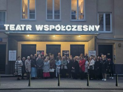 Grupa czytelników pozuje do zdjęcia stojąc przed budynkiem. Nad ich głowami widnieje napis Teatr Współczesny