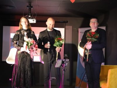 Natalia Srokocz i Jerzy Grzechnik stoją na scenie, trzymając w rękach wręczone im bukiety kwiatów. Obok nich stoi trzeci mężczyzna w okularach i garniturze, również trzymający bukiet. Artyści uśmiechają się w stronę publiczności