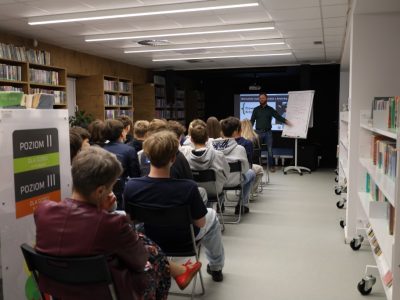 Krzysztof Piersa wskazuje ręką na flipchart z rysunkiem podczas warsztatów z młodzieżą w bibliotece