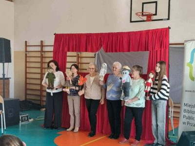 W centralnej części zdjęcia widać kobiety pozujące do zdjęcia. Każda z nich trzyma w dłoniach maskotkę, której podkładała głos w trakcie przedstawienia