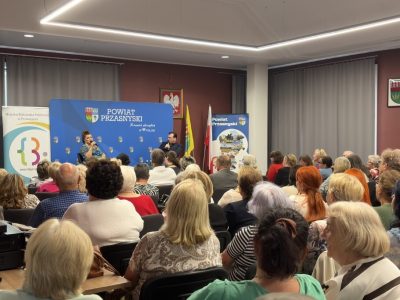 Szerokie ujęcie nowoczesnej, jasnej sali wypełnionej uczestnikami wydarzenia. Na samym końcu sali widać scenę, na której trwa rozmowa z Katarzyną Skrzynecką
