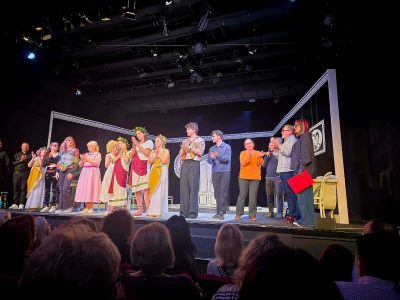 Aktorzy stoją na scenie teatru, gdzie są obserwowani przez widownię